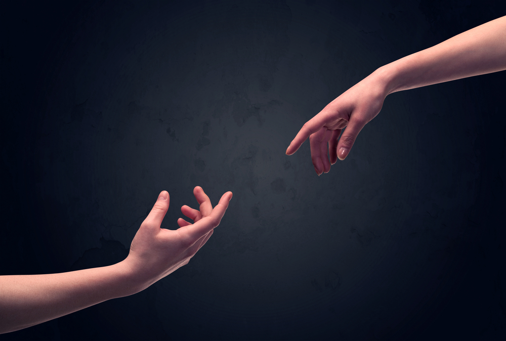 Two male hands reaching out to one another, almost touching, in front of dark clear empty background wall concept Two male hands reaching out to one another, almost touching, in front of dark clear empty background wall concept